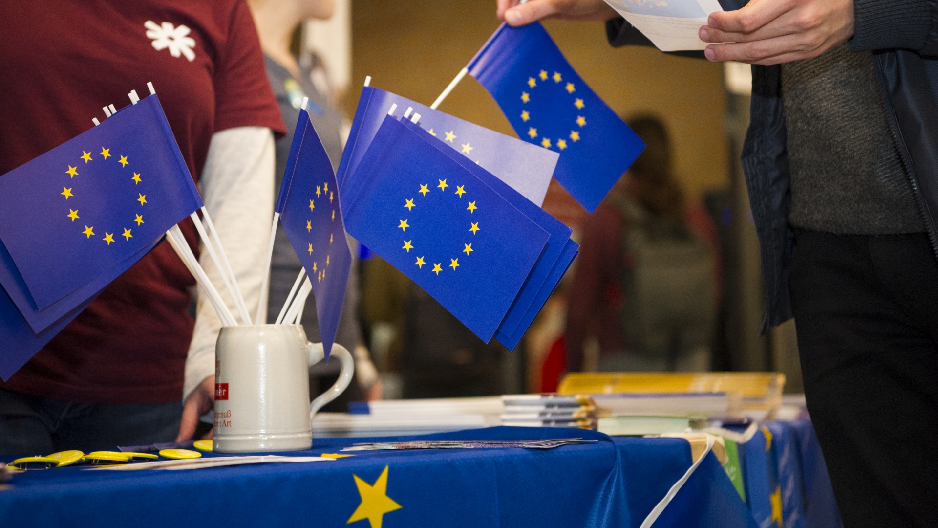 Eine Hand zieht aus einem Bierkrug kleine Europa-Flaggen heraus. 