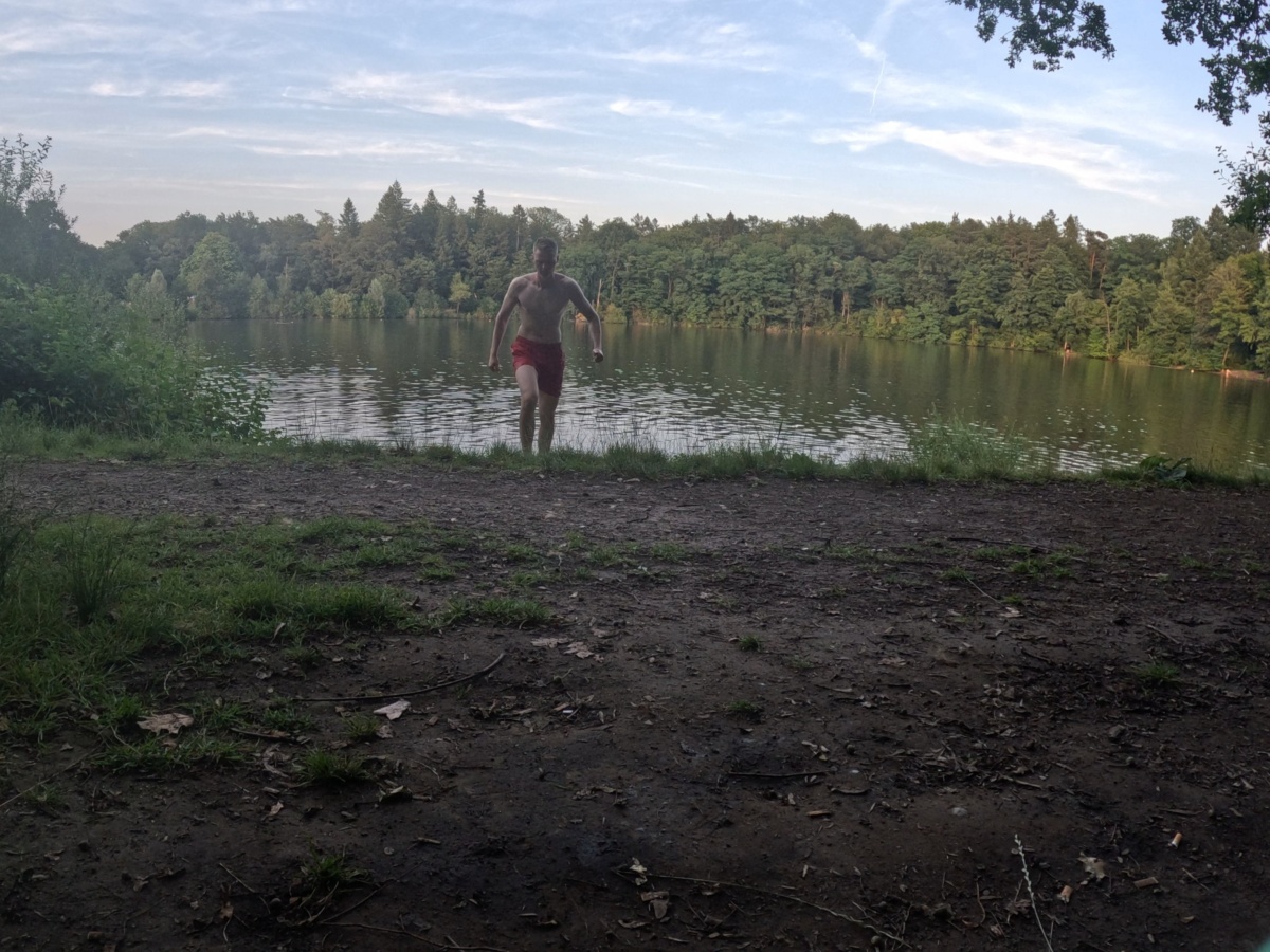 Arnd kommt mit roter Badehose aus einem See.