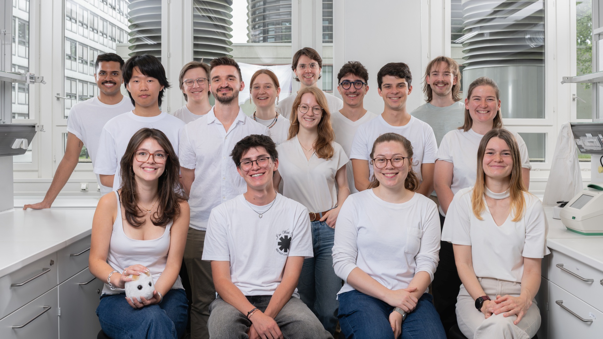 Group photo of a diverse team of researchers in a laboratory, all wearing white clothing.