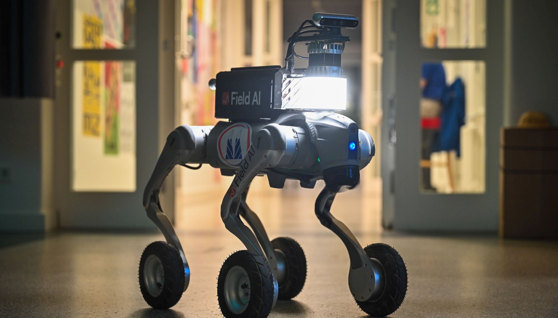 Autonomous four-wheeled robot with camera and sensors walking in a hallway.